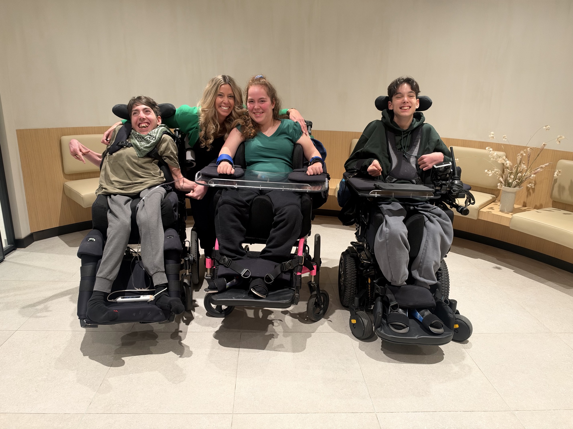 Dana Geall smiling with the triplets, who are seated in their wheelchairs